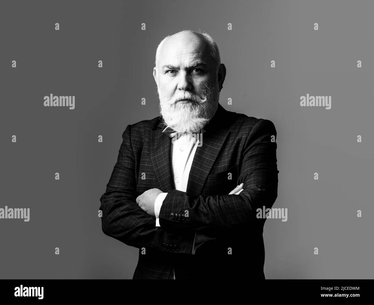 Seriöser älterer Mann in Anzug mit gekreuzten Armen. Bärtiger Mann mittleren Alters mit ernsthaftem Ausdruck in einem Nahaufnahme-Porträt von Kopf und Schultern. Stockfoto