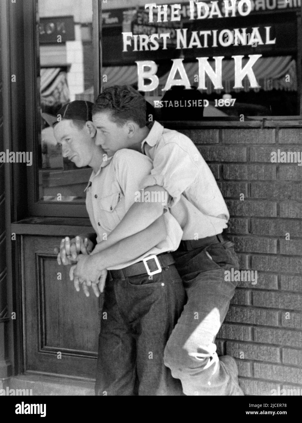 1941, Juni, CALDWELL, IDAHO, USA: Zwei JUNGEN FLIRTEN, in blauen Jeans-Hosen, umarmte wie sehr enge Freunde posieren und lächeln, lehnen sich am Eingang zu einem Bankbüro der IDAHO FIRST NATIONAL BANK of CALDWELL FILIALE. Foto von RUSSELL LEE ( 1903 - 1986 ), Mitarbeiter der United States Agricolture Farm Security Administration oder Office of war Information inländischen Fotoeinheiten, als ein Werk der US-Bundesregierung. - LIEBE - AMORE - STATI UNITI AMERICA - bellezza - Schönheit - LGBT - HOMOSEXUELL - STOLZ - JUGEND - Gioventù - Portrait - ritratto - omosessuale - Homosexualität Stockfoto