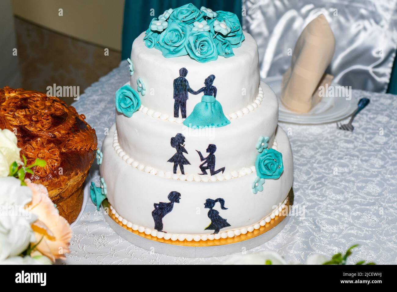 Wunderschöner Hochzeitstorte. Weißer dreistufiger Kuchen mit blauen Rosen und Figuren des Brautpaten Stockfoto