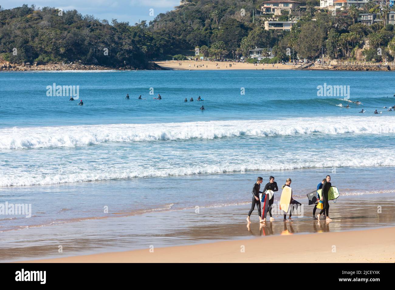 Manly Beach Sydney Teenager Jungen mit Bodyboards, Surfer im Meer und Shelly Beach in der Ferne, Sydney, NSW, Australien Stockfoto