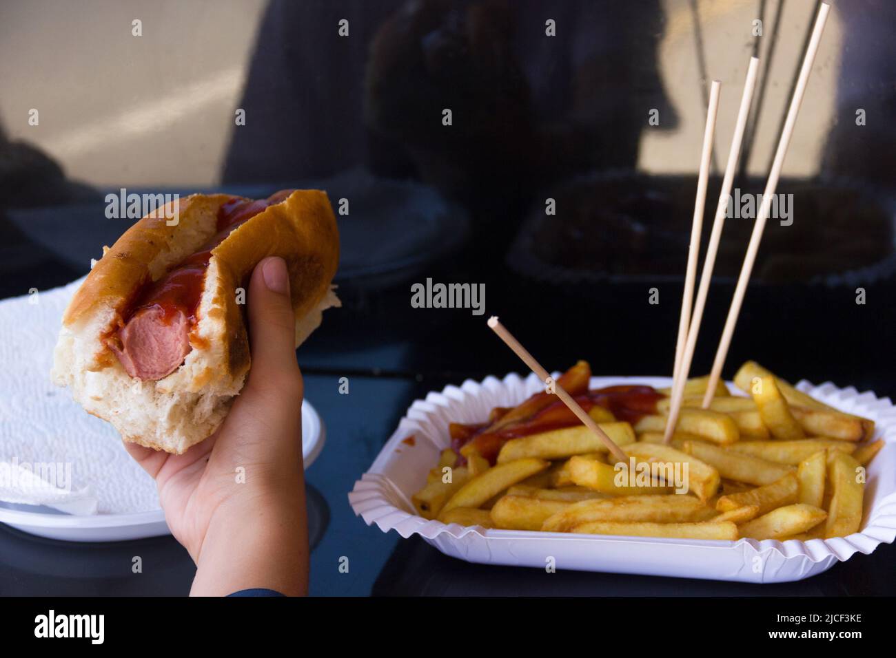 Hand halten Hot Dog von pommes frites Platte. Fast Food, ungesunde Ernährung, Ketchup-Sauce, leckere Konzepte Stockfoto