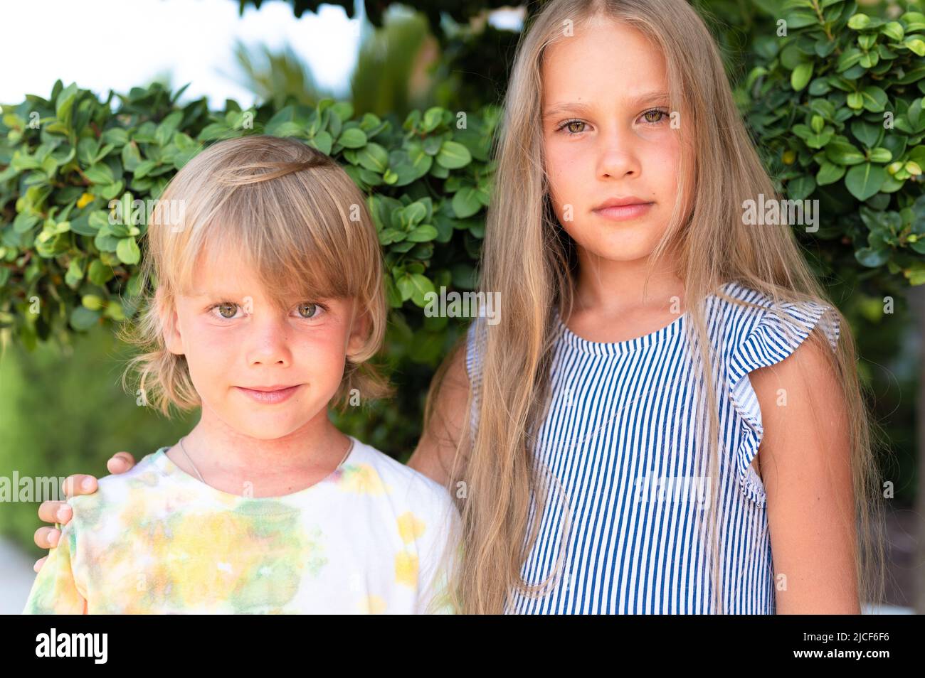 Glücklich Geschwister Kinder Reisende Junge Bruder von fünf Jahren und Mädchen Schwester von acht Jahre alten Freunden umarmt auf grünen Pflanzen Hintergrund und schauen in Stockfoto