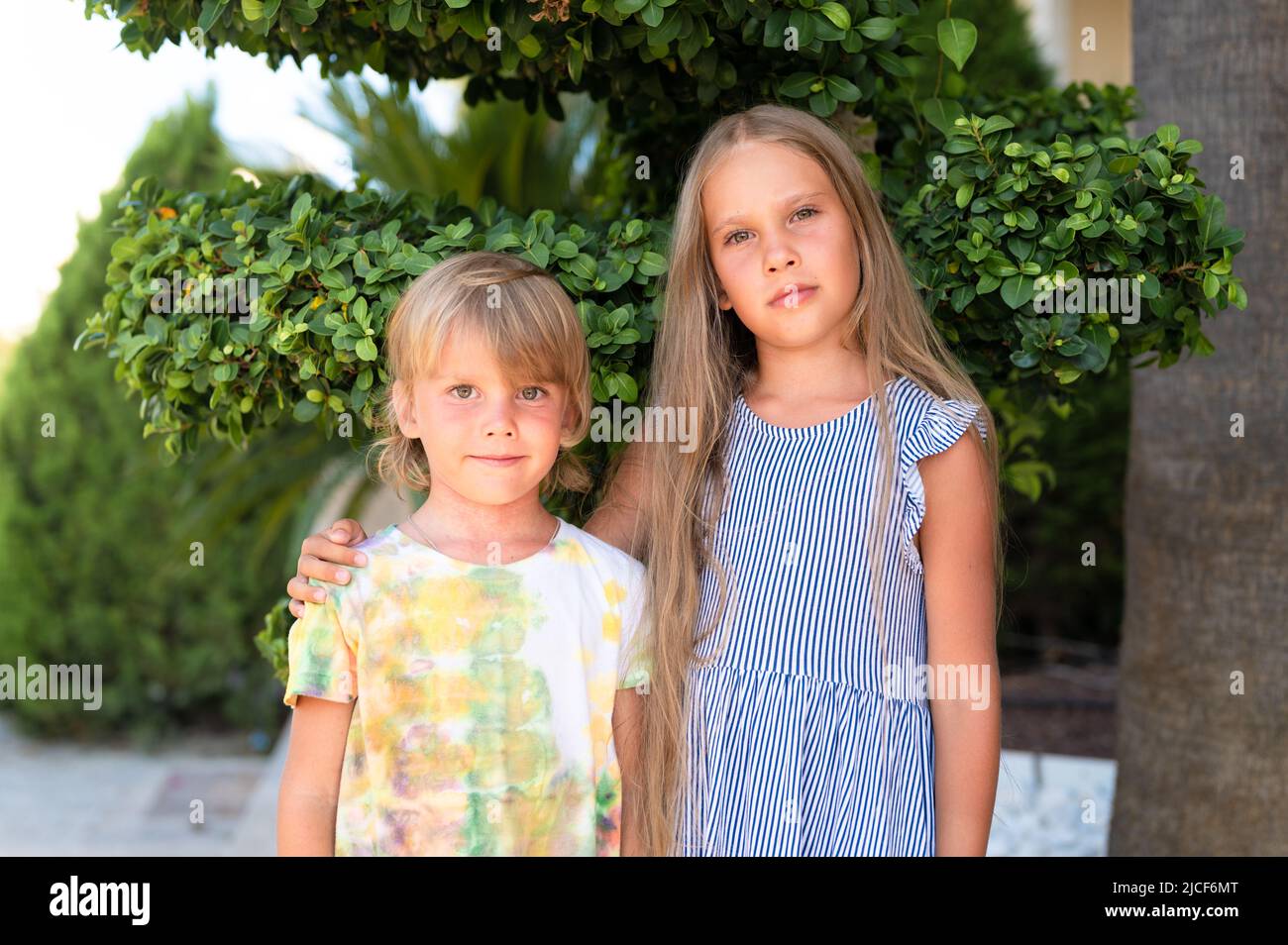 Glücklich Geschwister Kinder Reisende Junge Bruder von fünf Jahren und Mädchen Schwester von acht Jahre alten Freunden umarmt auf grünen Pflanzen Hintergrund und schauen in Stockfoto