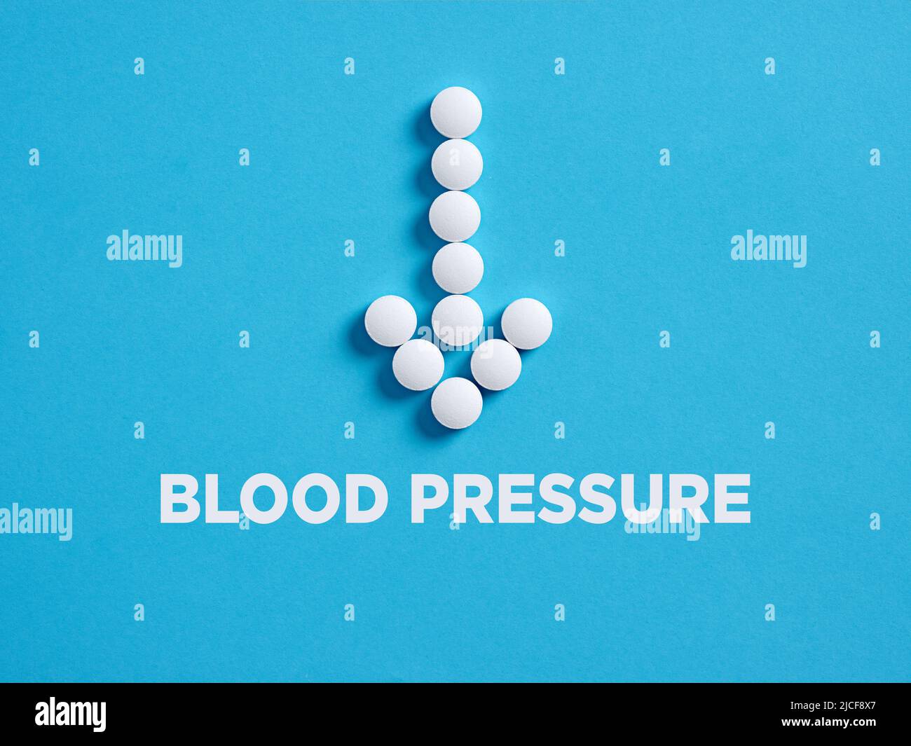 Runde weiße medizinische Pillen in Pfeilform, die auf das Wort Blutdruck zeigen. Behandlungskonzept zur Senkung des Blutdrucks. Stockfoto