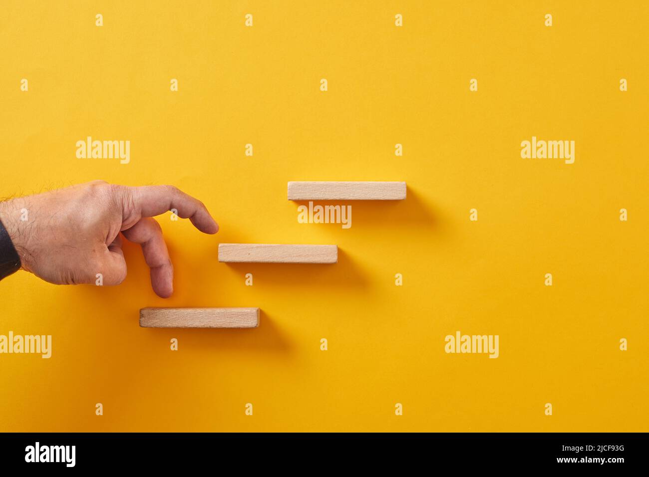 Männliche Hand klettert die hölzerne Würfeltreppe auf gelbem Hintergrund. Karriereziel, Geschäftserfolg und Entwicklungskonzept. Stockfoto