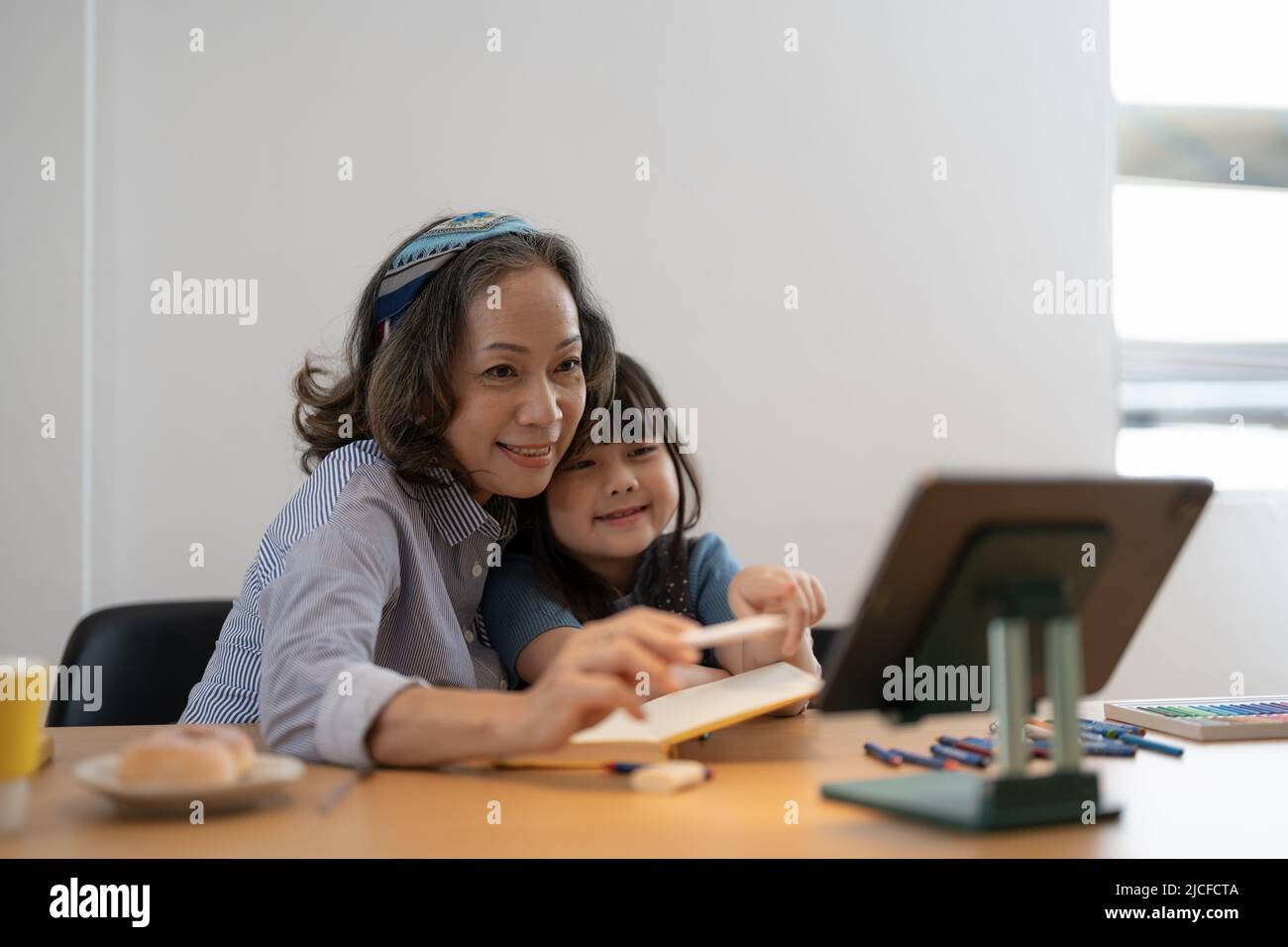 Liebevolle ältere Großmutter umarmt Schultern von kleinen Mädchen Enkelkind helfen bei der Vorbereitung Hausaufgaben Unterstützung geben Ratschläge. Freundliche, ältere Lehrerin Stockfoto