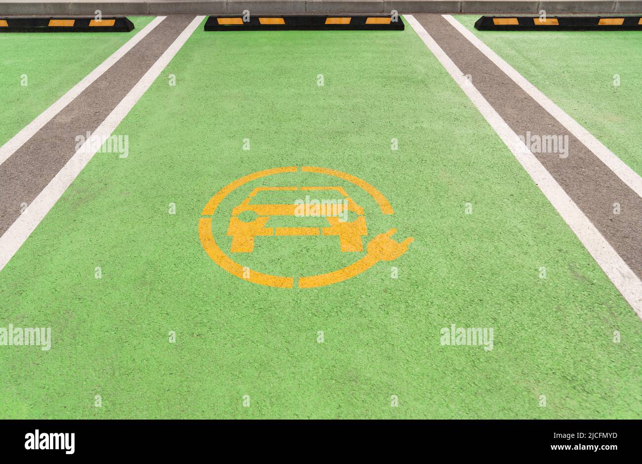 Gelbes Elektroauto-Symbol auf grünem Asphalt. Parkplatz für Elektrofahrzeuge Stockfoto