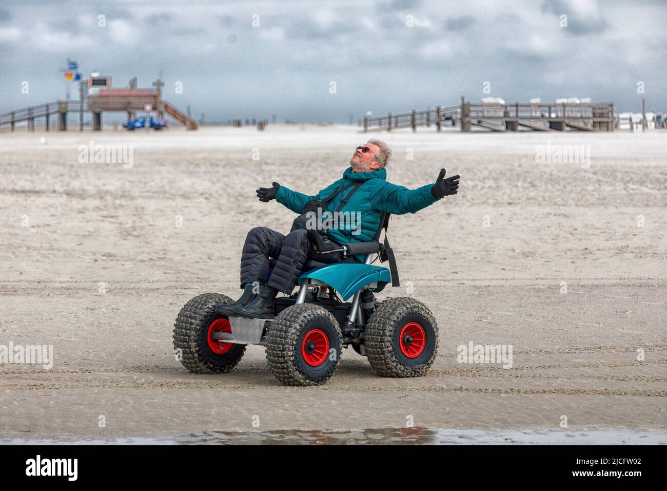Mann im Strandrollstuhl, ragt vor Freude die Arme, Sankt-Peter-Ording, Schleswig-Hostein, Deutschland Stockfoto