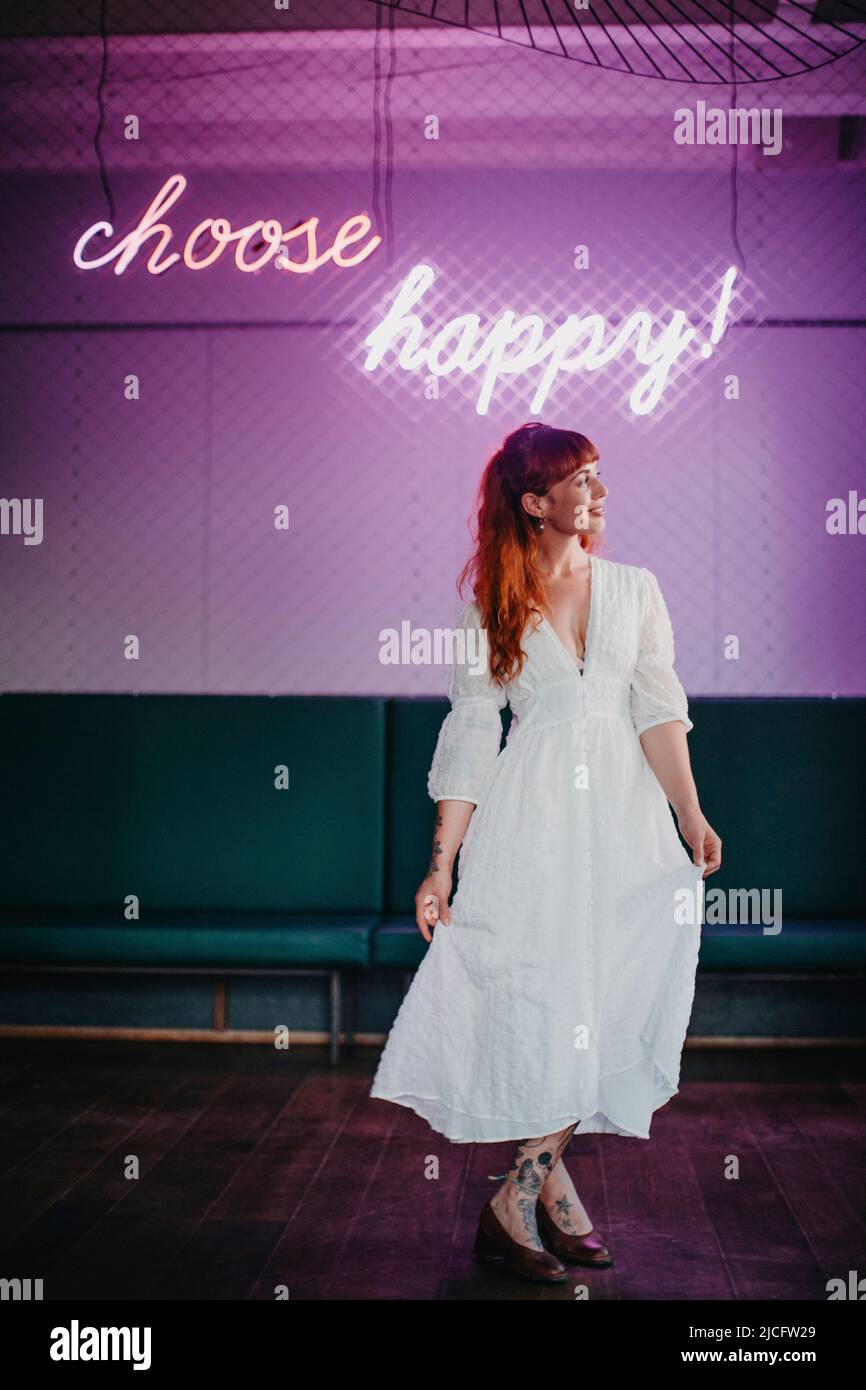 Junge Frau, die unter dem Neonschild „choose happy!“ lappt Stockfoto
