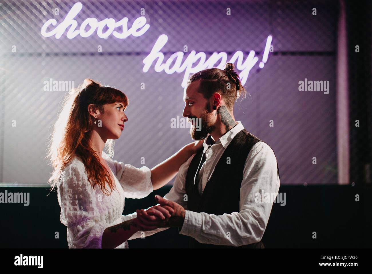 Junges verliebte Paar tanzt unter einem Neonschild „choose happy!“ Stockfoto