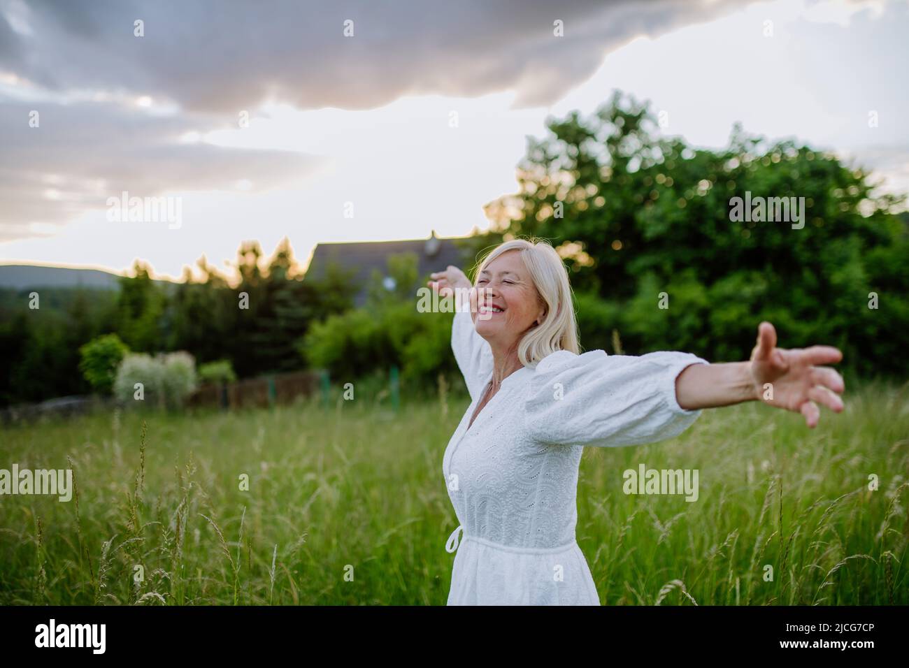 Ältere Frau mit ausgestreckten Armen und Gesicht nach oben im Park am Sommertag, psychische Gesundheit Konzept. Stockfoto