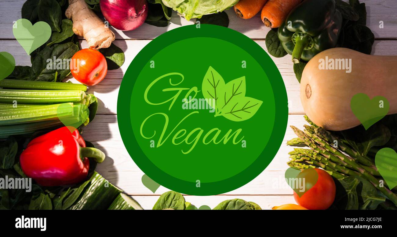 Bild von GO vegan Text in grün mit Laub-Logo, über frischem Gemüse auf weißen Brettern Stockfoto