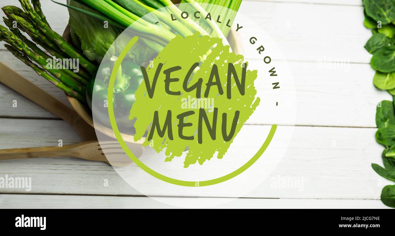 Bild von lokal angebauten veganen Menütext in grün, über Schüssel mit frischem Gemüse auf weißen Brettern Stockfoto
