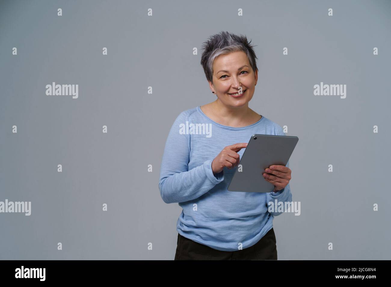 Reife grauhaarige Geschäftsfrau mit digitalem Tablet in den Händen, die online arbeitet. Hübsche Frau im Jahr 50s in blauer Bluse isoliert auf weiß. Ältere Menschen und Technologien. Stockfoto