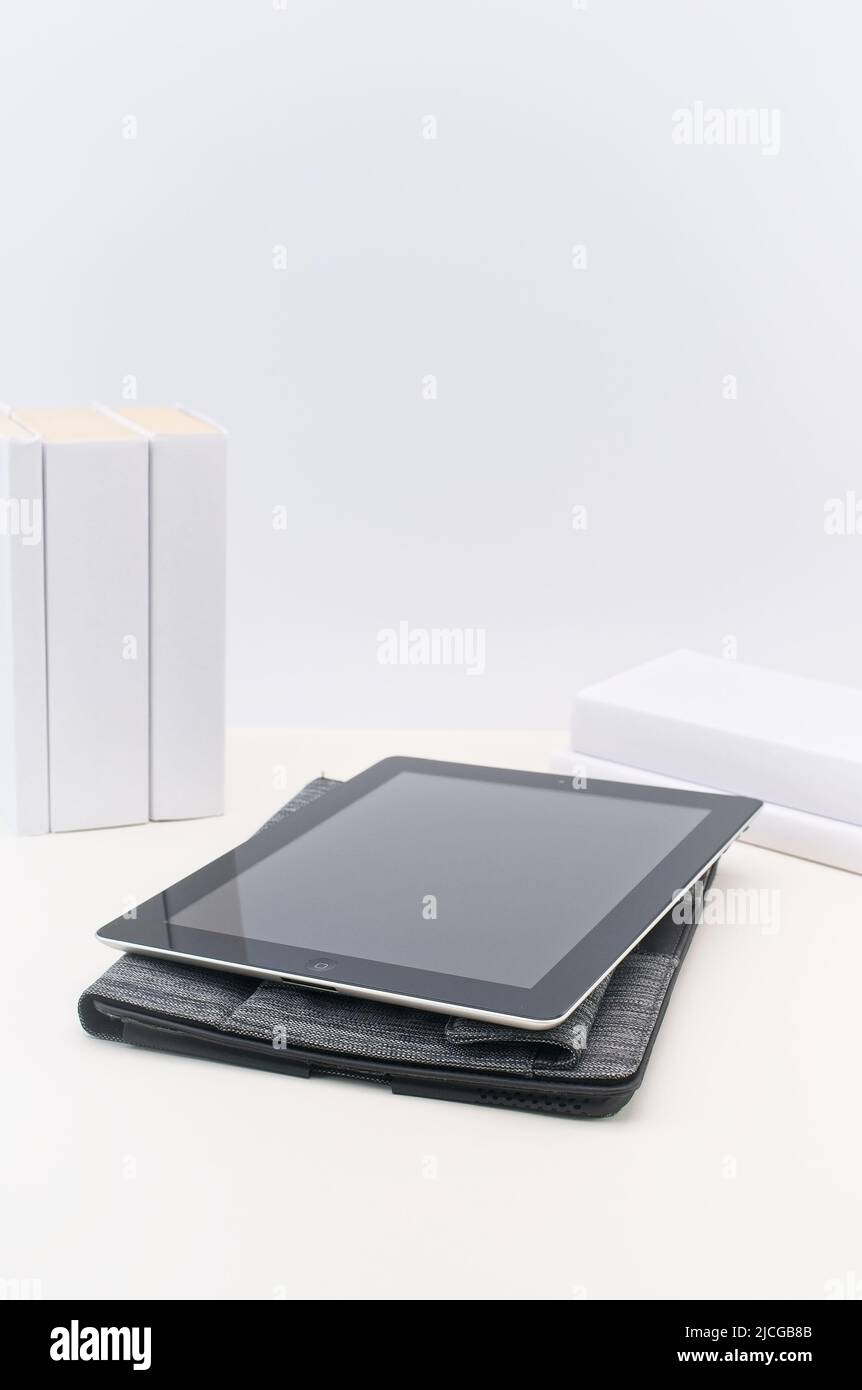 Apple ipad der ersten Generation, Fall auf einem hellen Schreibtisch mit Büchern an einer weißen Wand Stockfoto