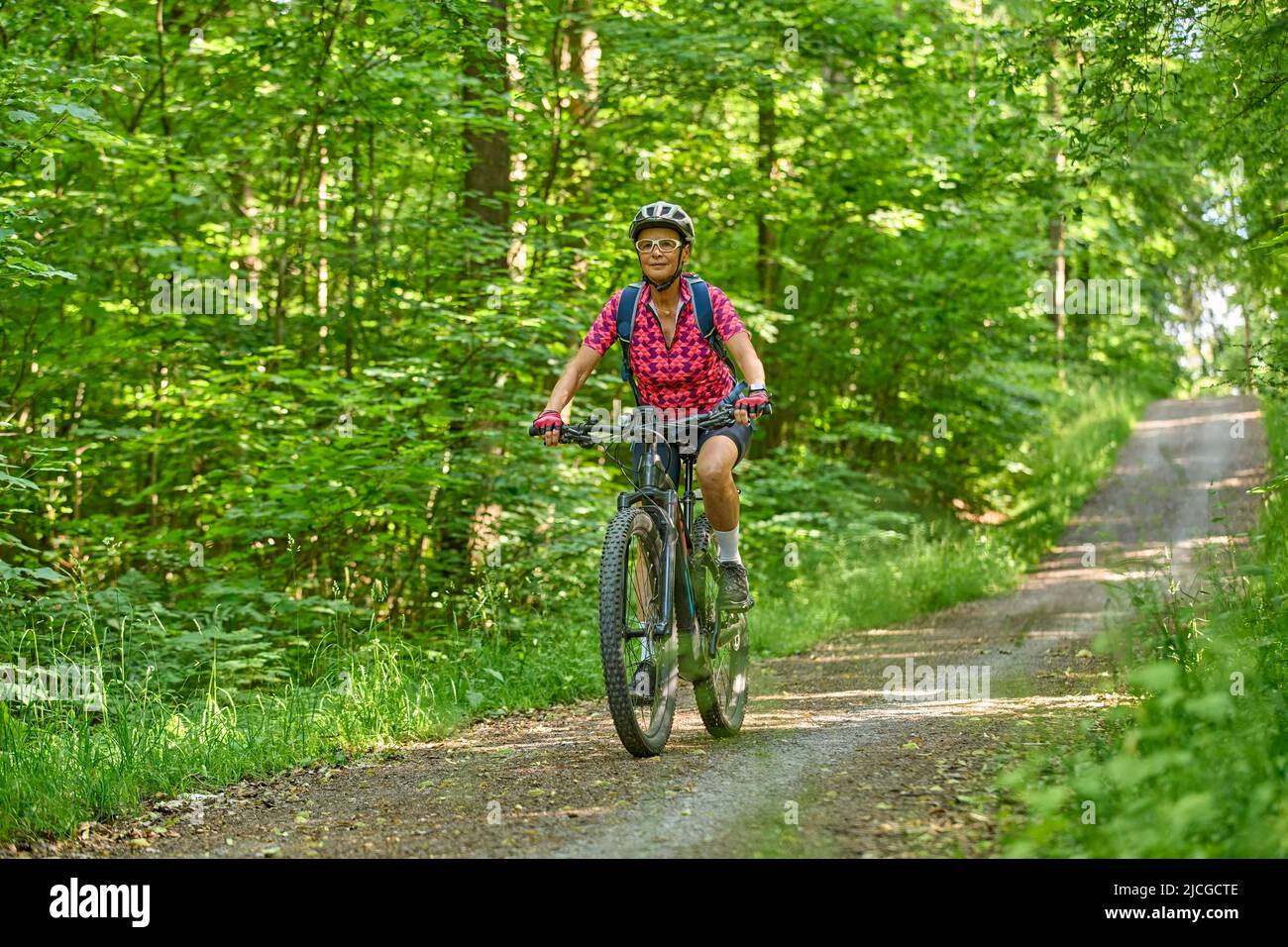Nette aktive ältere Frau, die mit ihrem elektrischen Mountainbike im grünen Stadtwald von Stuttgart unterwegs ist Stockfoto