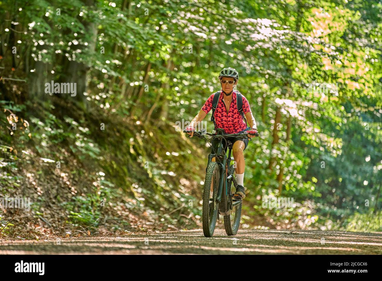 Nette aktive ältere Frau, die mit ihrem elektrischen Mountainbike im grünen Stadtwald von Stuttgart unterwegs ist Stockfoto