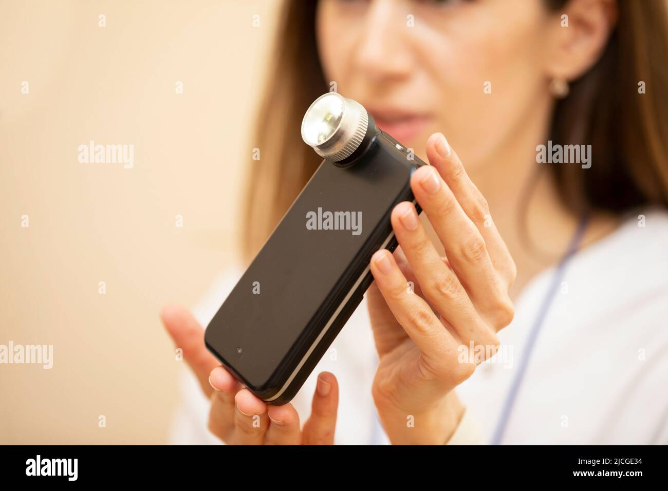 Ein Dermatologe zeigt ein modernes Gerät mit Licht, einer Telefonanwendung und einer Kamera, um Muttermale und Muttermale zu untersuchen. Stockfoto