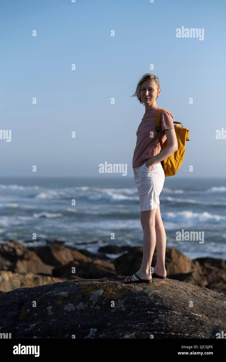 Eine Frau mit Rucksack steht auf den Felsen am Meer. Stockfoto