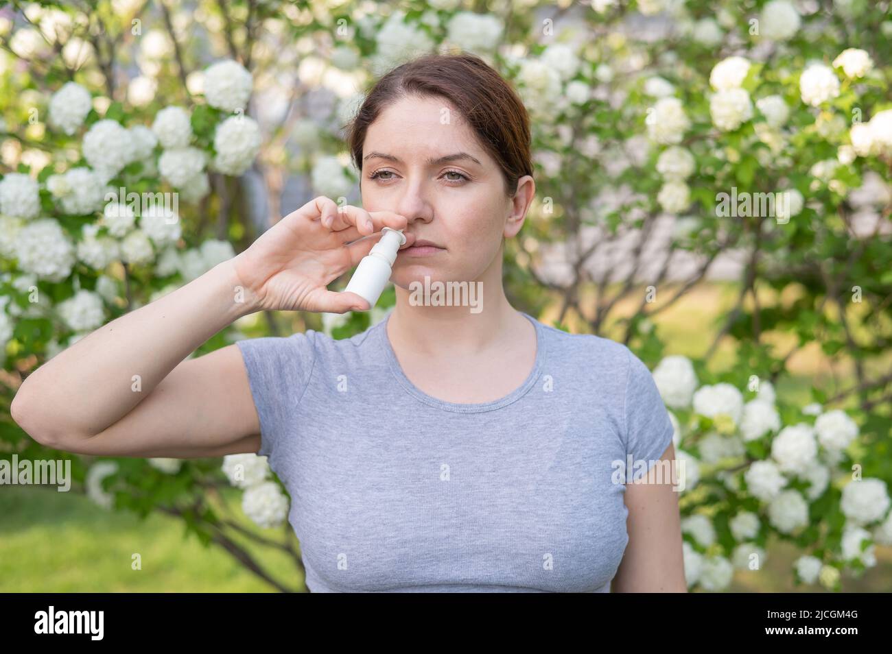 Kaukasische Frau verwendet ein Nasenspray, während sie im Park spazieren geht. Stockfoto