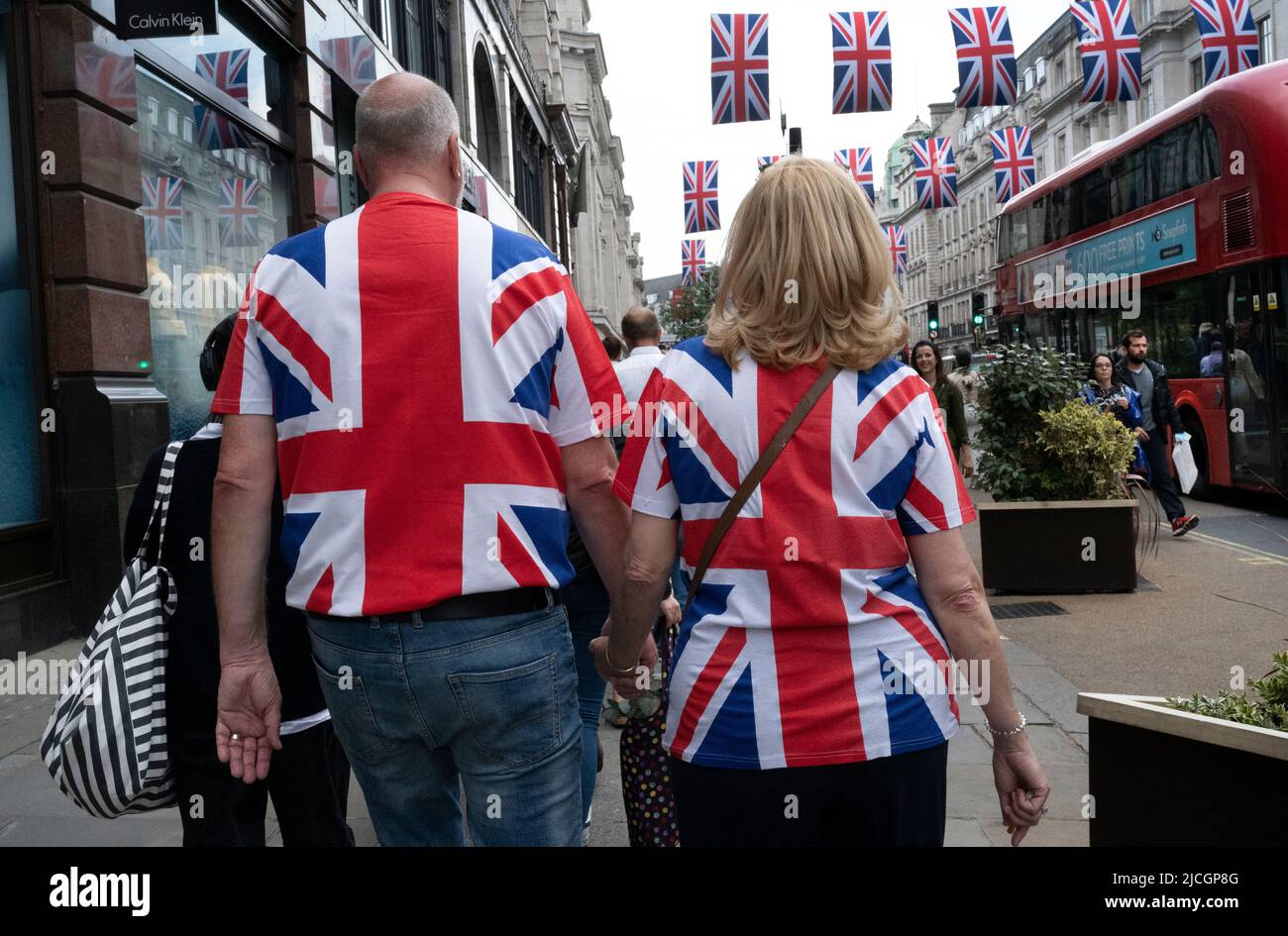 Im Zentrum von London, ein Paar mit Union Jack Tops, geht die Regent Street entlang, dekoriert mit Union Jacks. Stockfoto