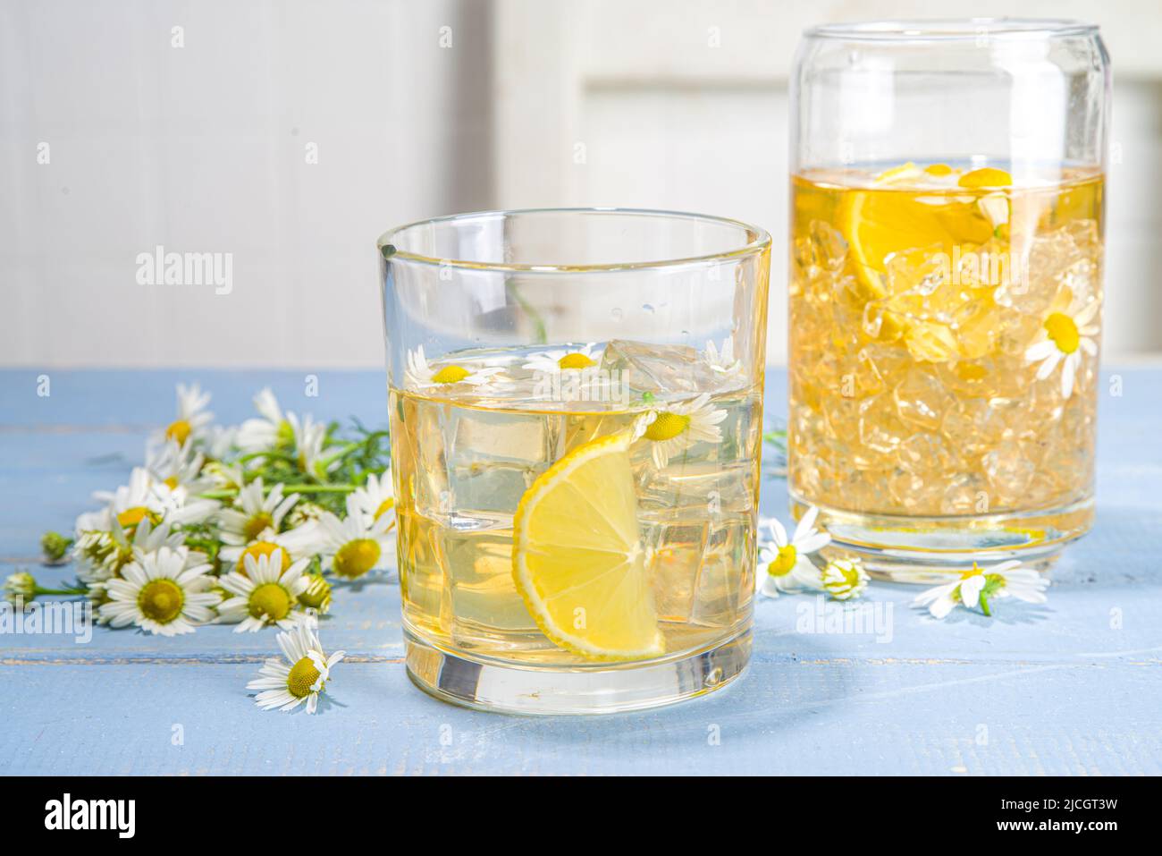 Pflanzliches organisches kaltes Getränk. Infundiert mit Blumenwasser. Iced Daisy Kamille Tee oder Limonade mit Zitronenscheibe und Eiswürfeln, in zwei verschiedenen Gläsern, blau w Stockfoto