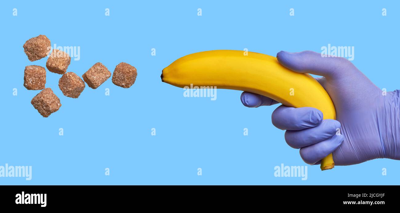 Eine Hand in einem Latexhandschuh hält eine Banane, die Zucker schießt. Hoher Gehalt an schnellen Kohlenhydraten in süßen Früchten. Konzept der diabetischen Ernährung Stockfoto