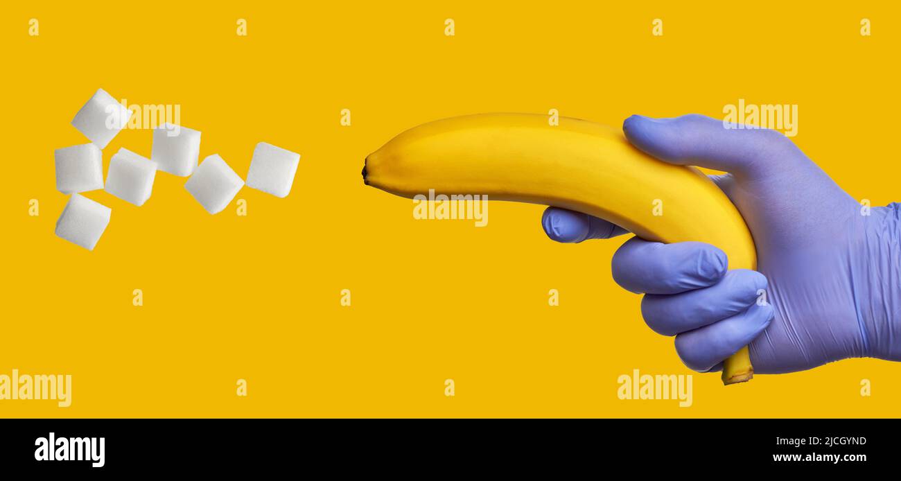 Eine Banane in der Hand in einem blauen medizinischen Handschuh schießt Zucker aus. Hoher Gehalt an schnellen Kohlenhydraten in süßen Früchten. Diabetes-Konzept Stockfoto