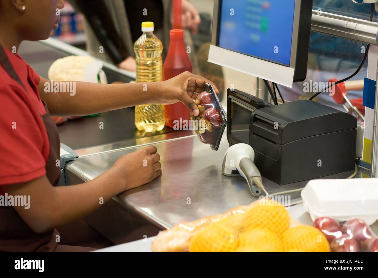 Hände einer jungen Verkäuferin, die verpackte Früchte und andere von den Käufern ausgewählte Lebensmittel im Supermarkt vor der Kasse scannt Stockfoto