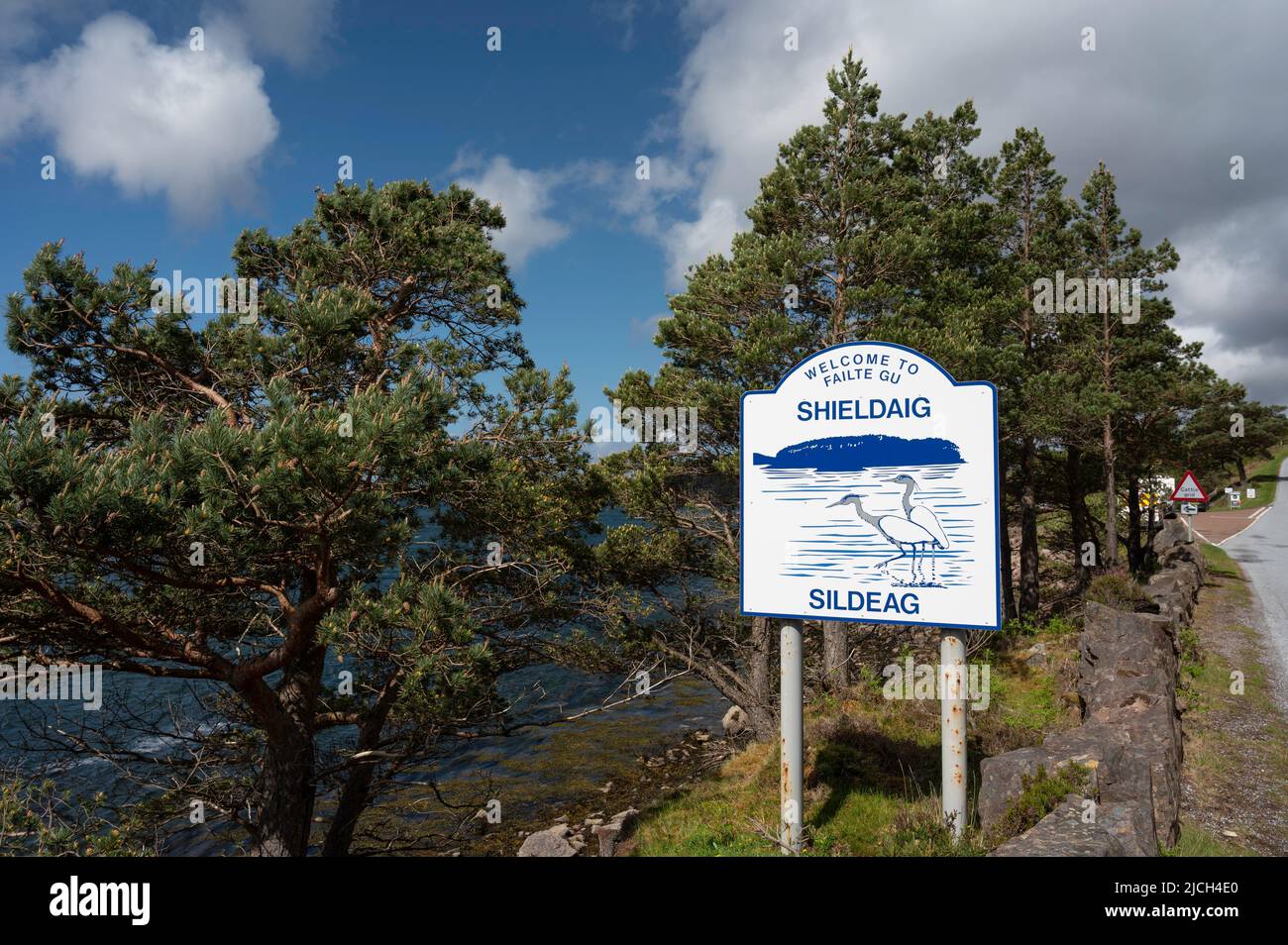 Willkommen bei Shieldaig Schild mit Hintergrund von Pinien. Blauer Himmel und Wolken, sonniger Tag. Keine Personen. Stockfoto