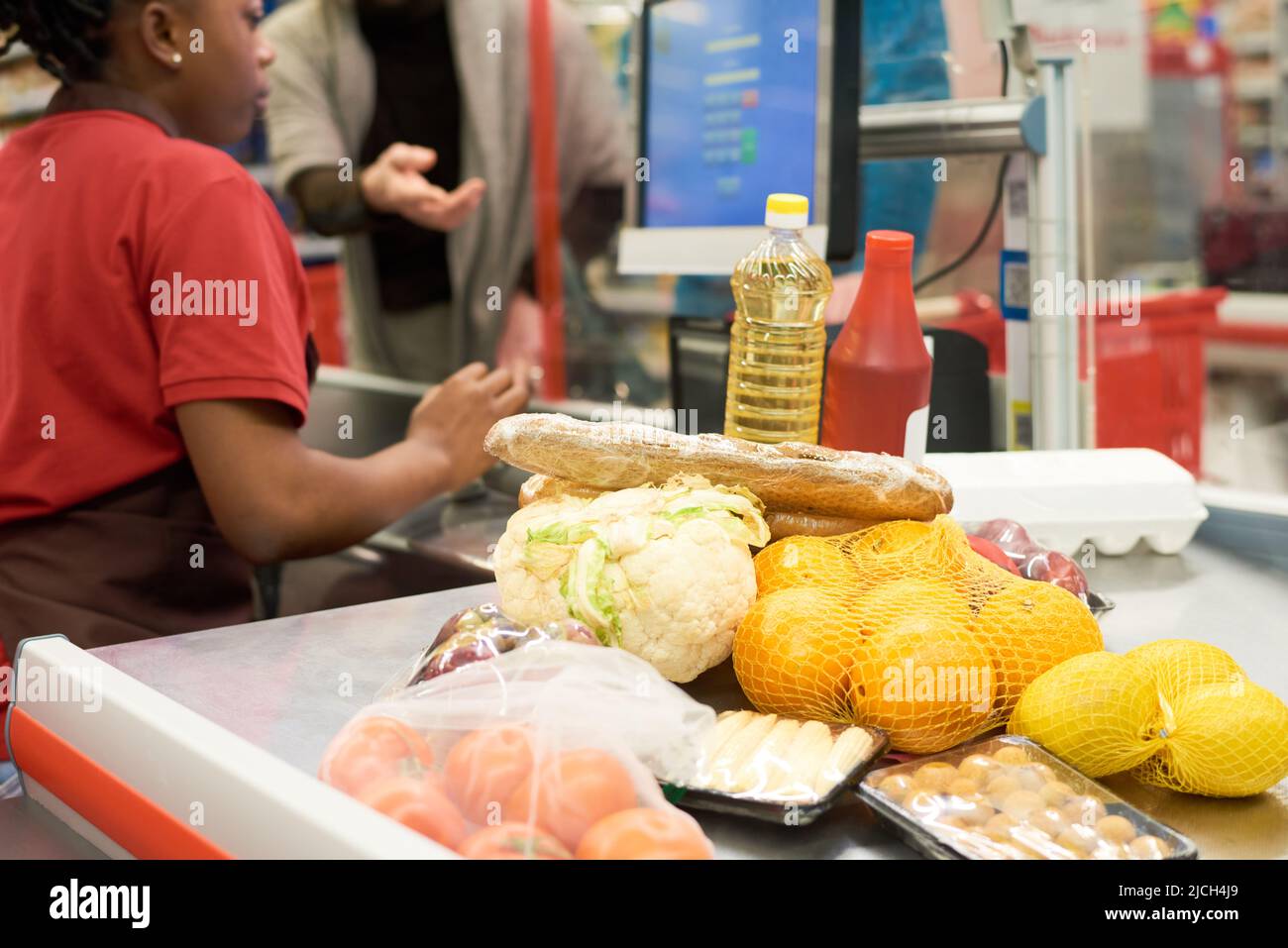 Frisch verpacktes Gemüse, Obst und andere Lebensmittelprodukte, die von einer Kassiererin gescannt wurden, die eine der Einkäufer im Supermarkt bedient Stockfoto