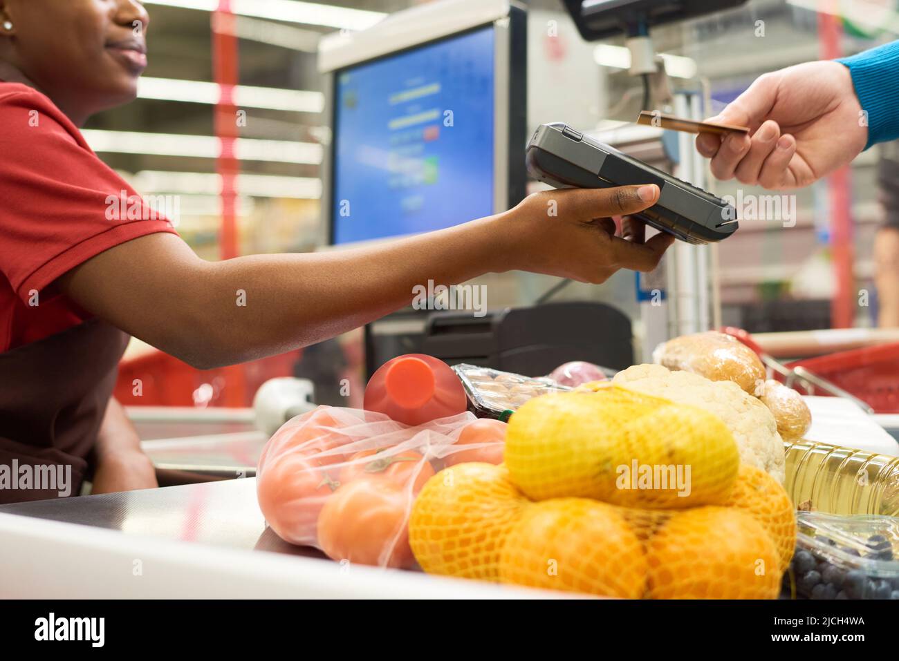 Junge schwarze Frau mit Zahlungsterminal, während der Käufer mit Kreditkarte für gekaufte Lebensmittel im Supermarkt bezahlt Stockfoto