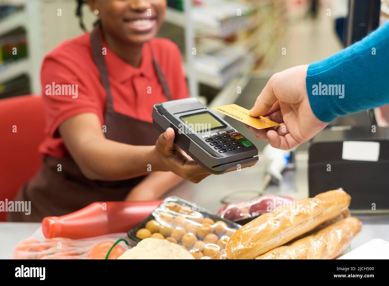 Käufer mit Kreditkarte über die Bezahlung am Terminal, die von einem jungen lächelnden Verkäuferin beim Kauf von Lebensmittelprodukten im Supermarkt gehalten wird Stockfoto