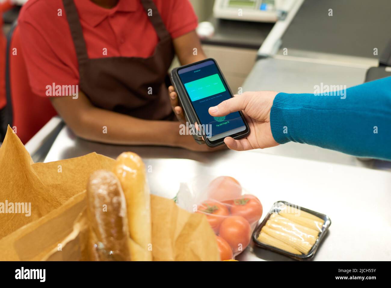 Der junge Afroamerikaner hält ein Zahlungsterminal während der kontaktlosen Bezahlung von Lebensmitteln durch den Verbraucher mit dem Smartphone Stockfoto