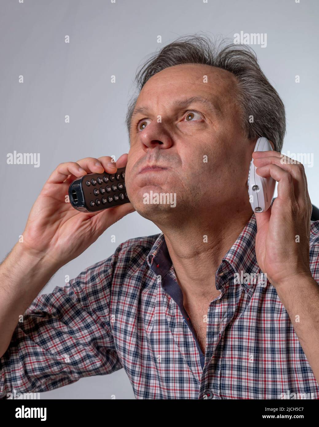 Ein Mann mit zwei Telefonen hat die Nase voll davon, über das Telefon mit unerwünschten Geschäftsvorschlägen belästigt zu werden Stockfoto