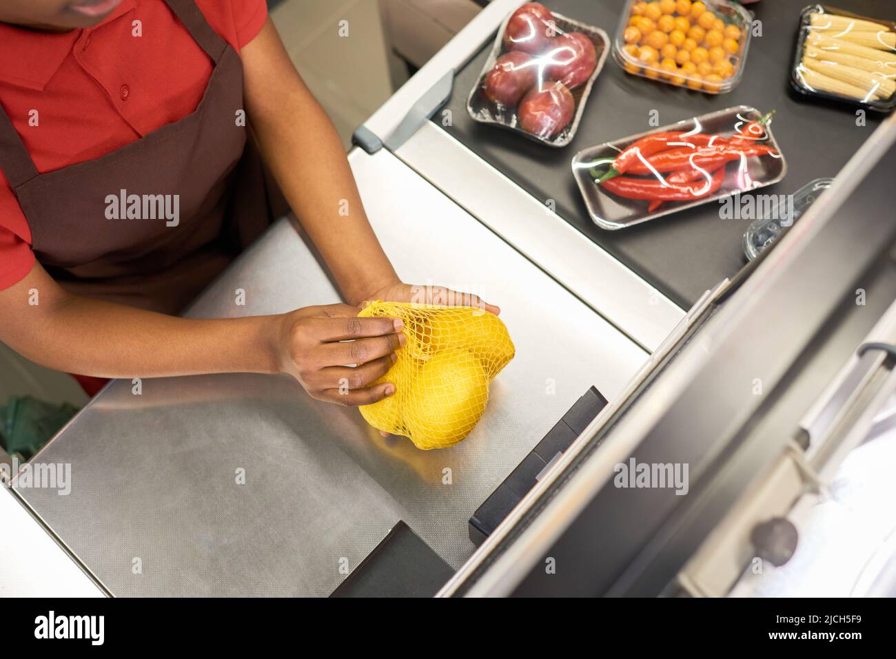 Über dem Winkel einer jungen afroamerikanischen Verkäuferin, die gepackte Zitronen über die Theke hält, sie wiegt und scannt Stockfoto