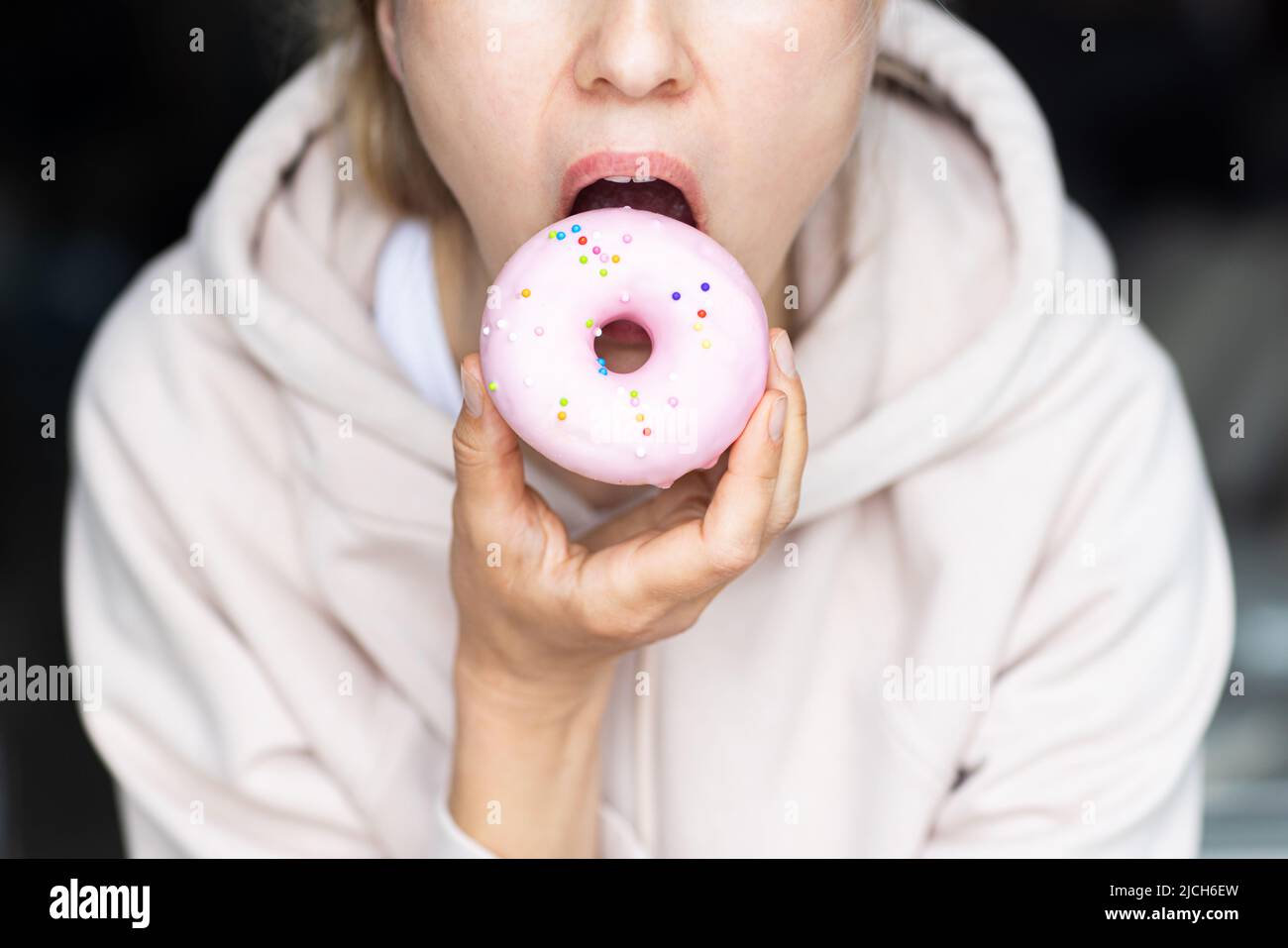 Nicht erkennbare junge Frau, die zu Hause in der Küche rosa Donut isst Stockfoto