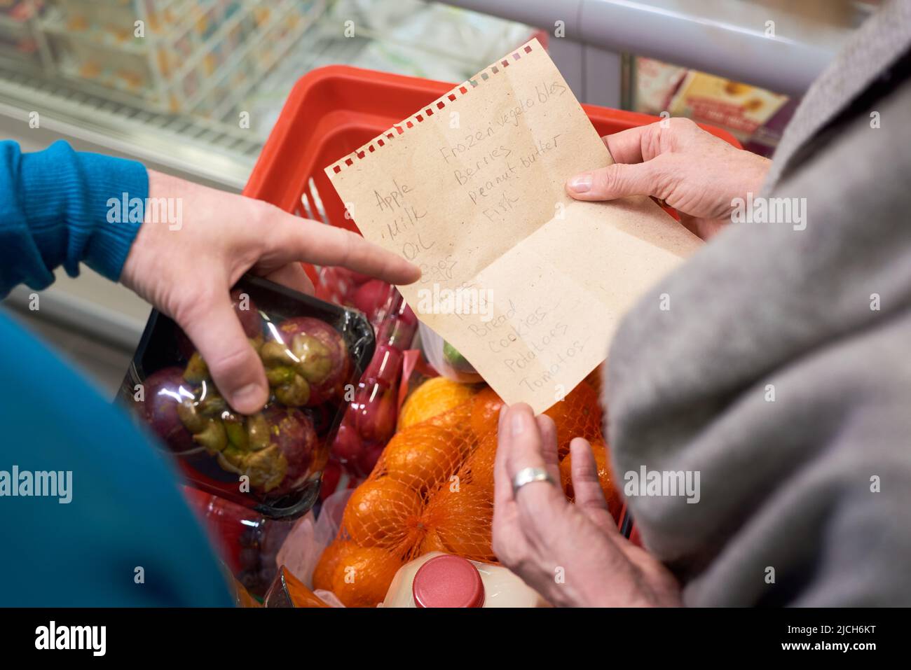 Übersicht über die Hand eines reifen Mannes, der auf die Einkaufsliste seiner Frau über den Wagen mit frisch verpackten Früchten und anderen Lebensmitteln zeigt Stockfoto