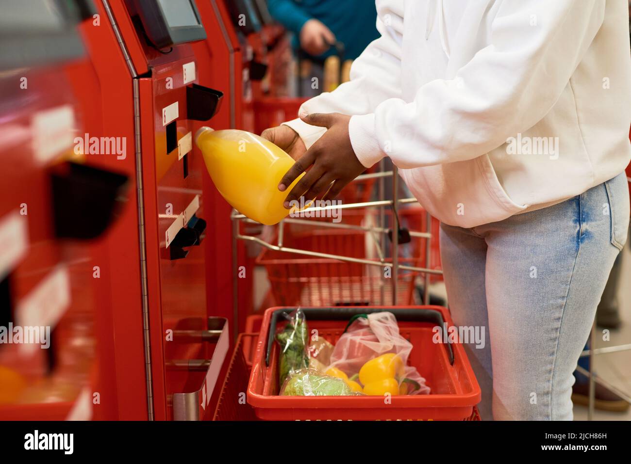 Weibliche Verbraucherin in der Freizeitkleidung scannt ausgewählte Lebensmittel im Selbstbedienungsterminal, während sie Getränke, Obst und Gemüse kauft Stockfoto