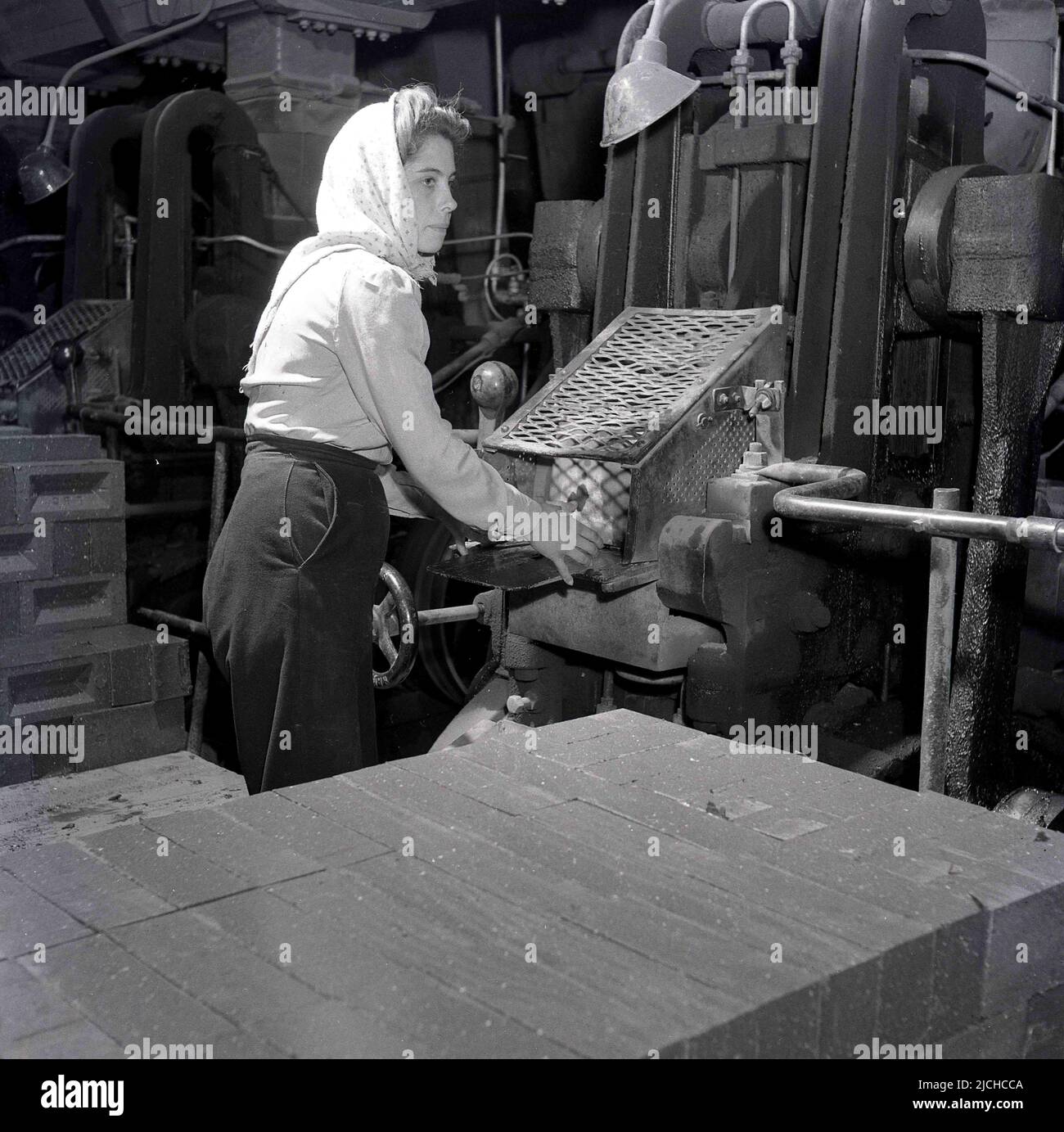 1950s, historisch, eine Frau in einem Kopftuch, die an Maschinen stand und dabei arbeitete, Ziegelsteine mit Ofen zu verarbeiten, bei der London Brick Company, Bedford, England, Großbritannien. Stockfoto
