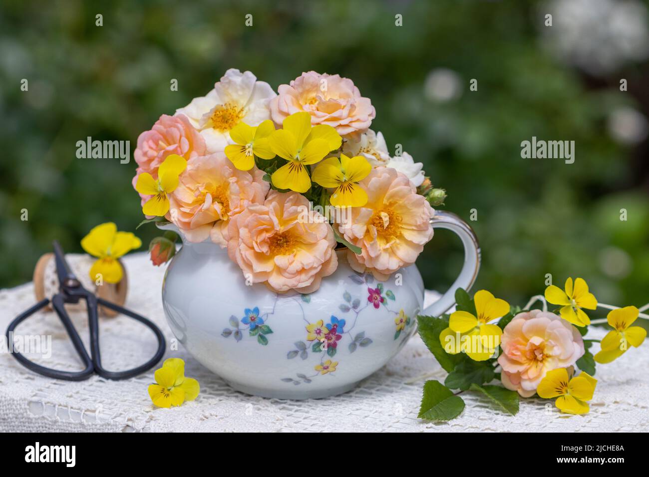 Bouquet von Aprikosenrosen und gelben Viola-Blüten in Jahrgangsmilchkanne Stockfoto