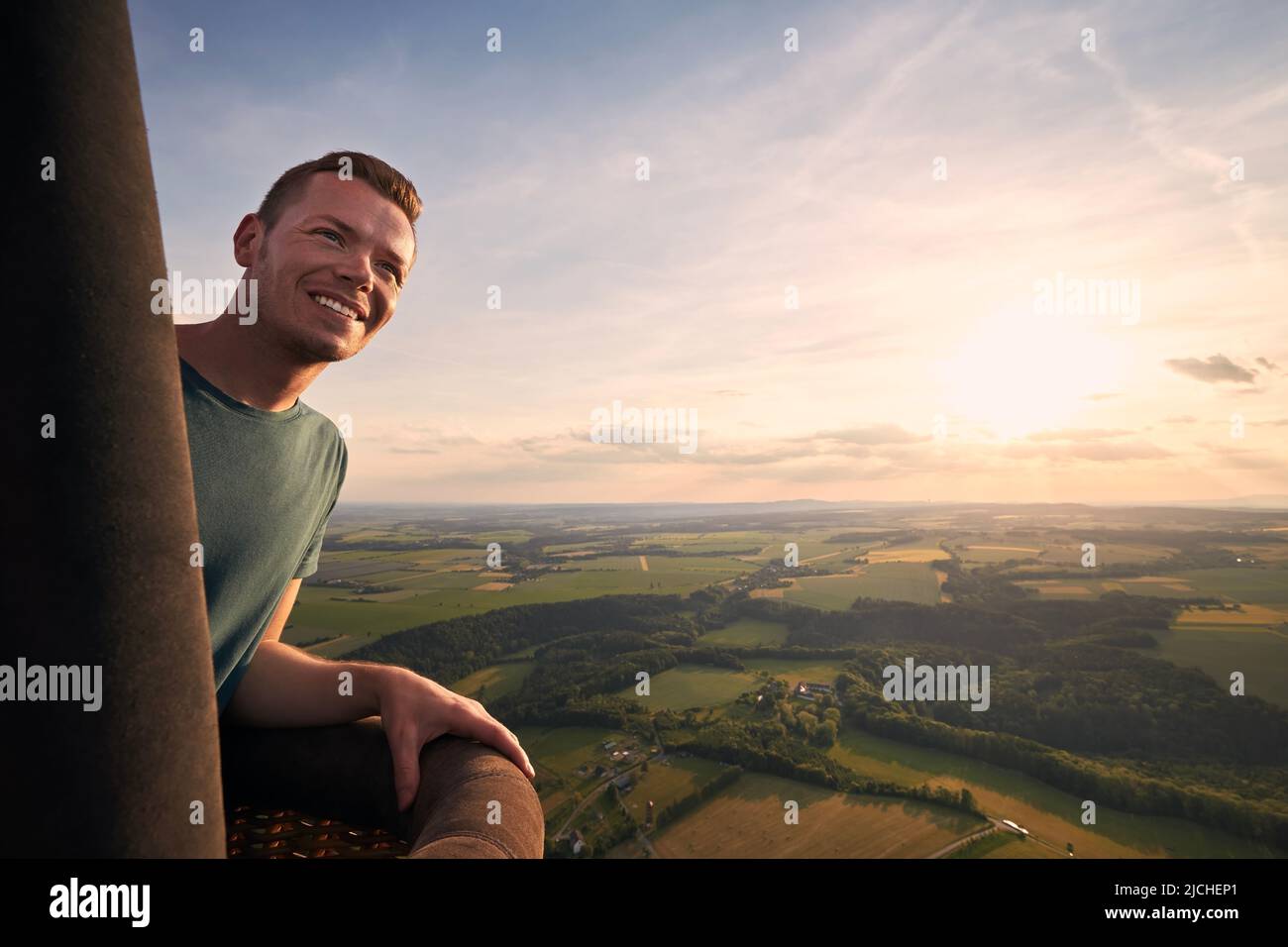 Mann, der den Blick vom Heißluftballon während des Fluges über die wunderschöne Landschaft bei Sonnenuntergang genießt. Themen Abenteuer, Freiheit und Reisen. Stockfoto