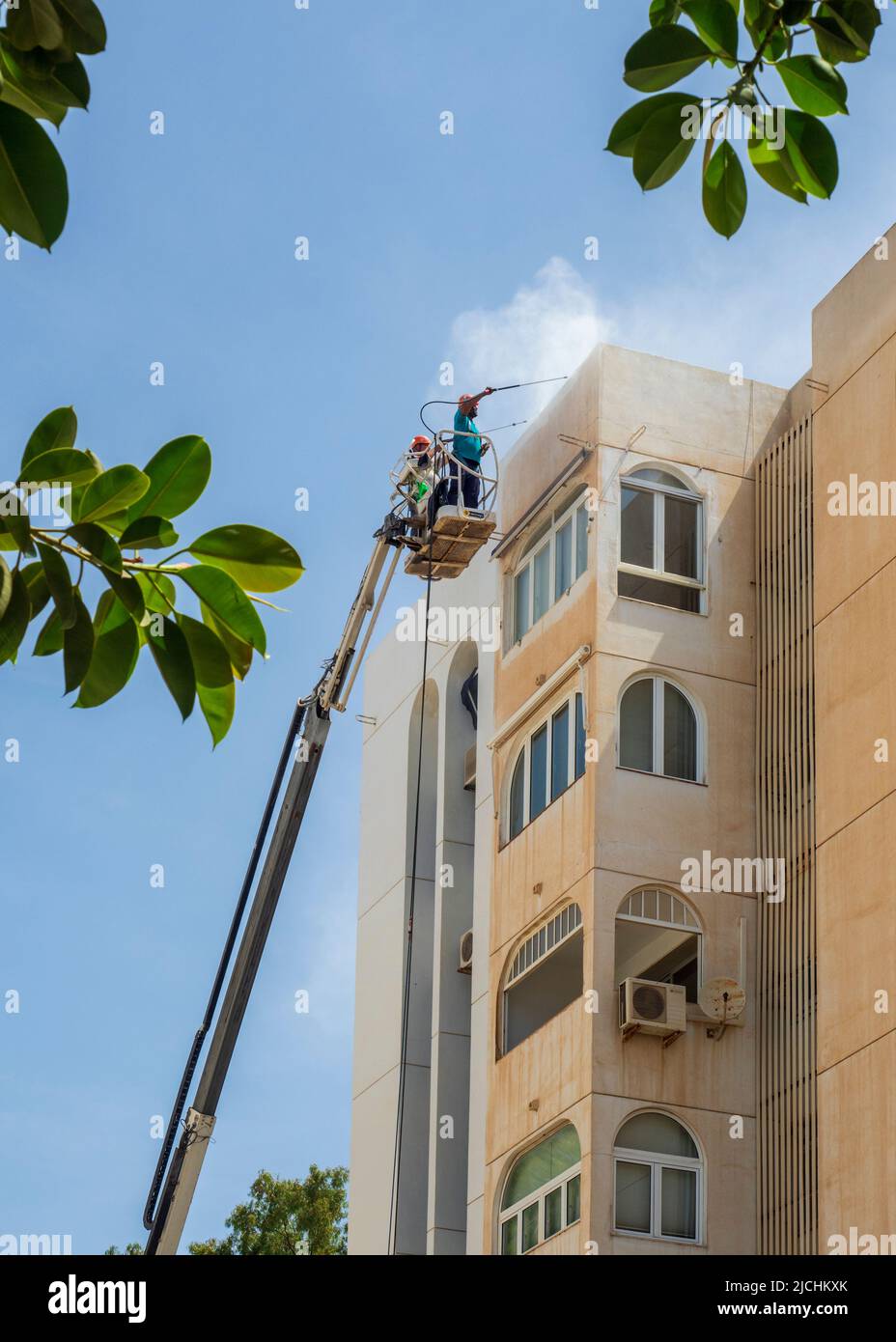 Ein Arbeiter auf einem Kran, der Staub aus der Wüste an der Fassade eines Gebäudes in Malaga reinigt. Stockfoto