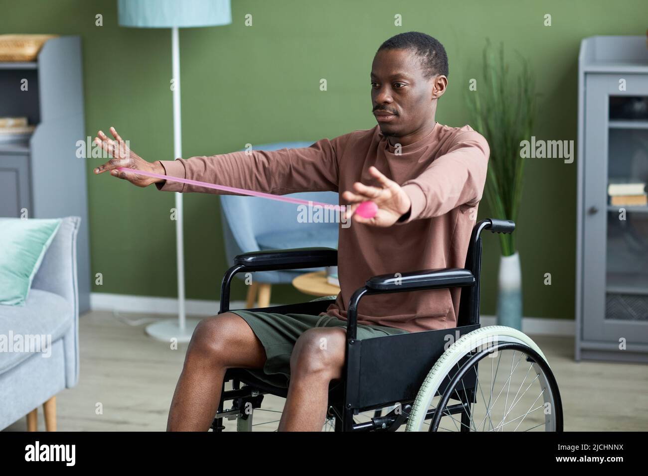 Porträt eines erwachsenen afroamerikanischen Mannes mit Behinderung, der zu Hause mit Gummis trainiert Stockfoto