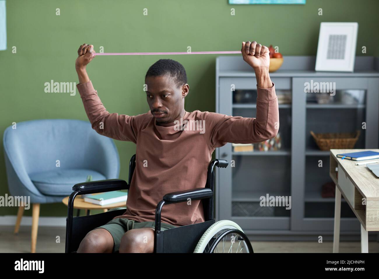 Minimalporträt eines erwachsenen schwarzen Mannes mit Behinderung, der zu Hause mit Gummis trainiert Stockfoto
