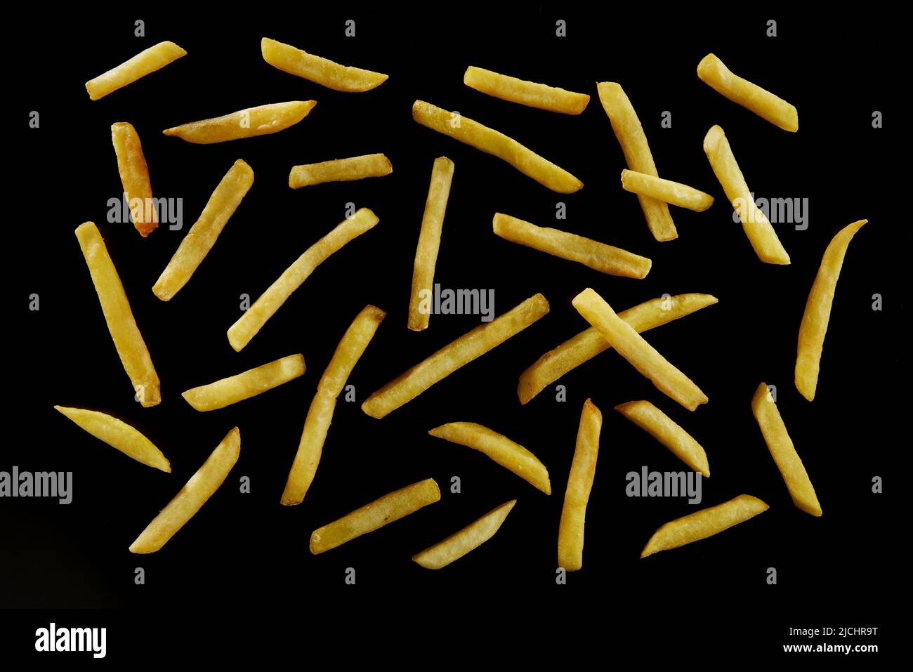 Draufsicht auf appetitlich knusprige Pommes frites, die auf schwarzer Oberfläche als abstrakter Hintergrund verstreut sind Stockfoto