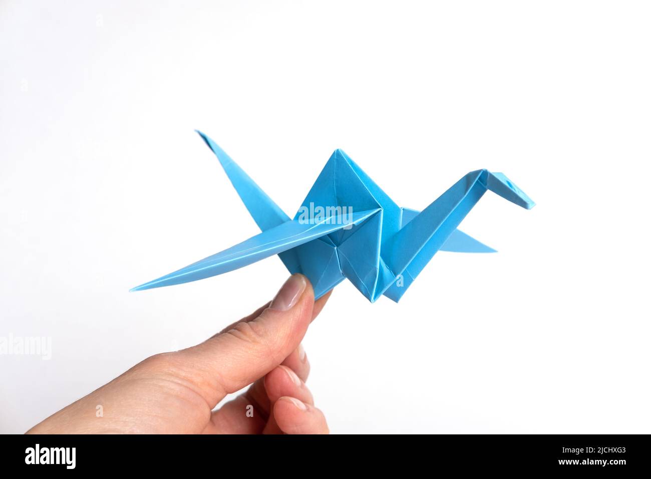Hand hält Papier blauen Vogel isoliert auf weißem Hintergrund. Papierkran als Symbol des Friedens. PapierOrigami. Papierhandwerk mit Kindern. Stockfoto