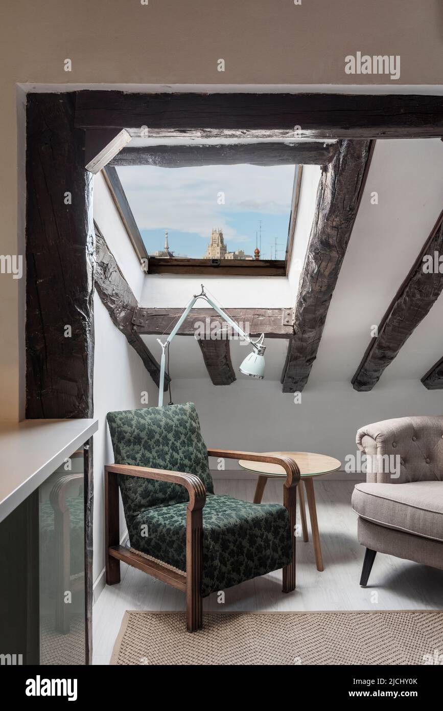 Ecke eines Zimmers in einer Dachgeschosswohnung mit schrägen Decken mit freiliegenden Holzbalken und einem Dachfenster mit Blick auf die Stadt Stockfoto