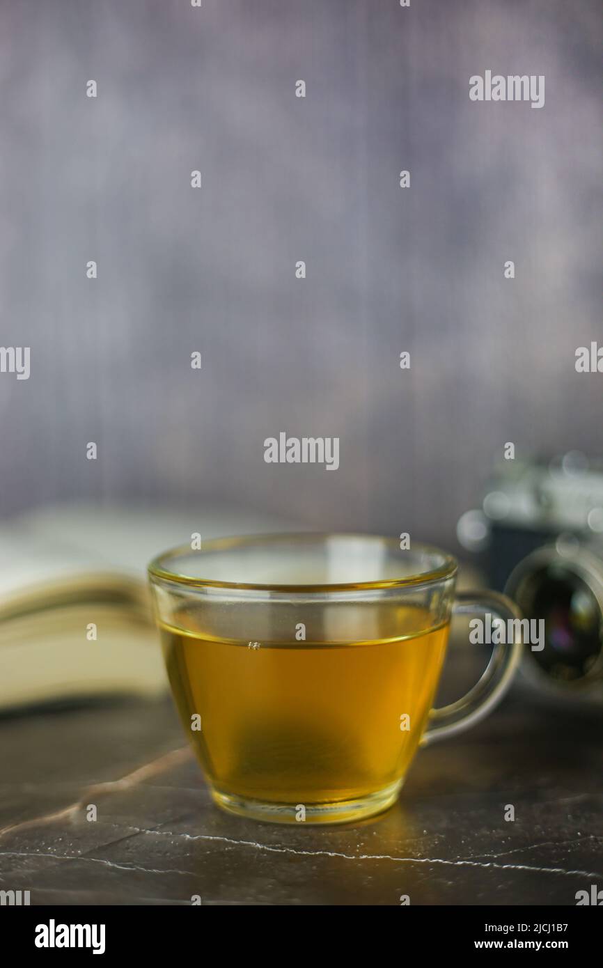 Gebrauter grüner Kräutertee in transparenter Tasse in der Nähe von offenem Buch und Vintage-Kamera auf dunklem Hintergrund Stockfoto Gebrauter grüner Kräutertee in transparenter Tasse in der Nähe von offenem Buch und Vintage-Kamera auf dunklem Hintergrund Stockfoto