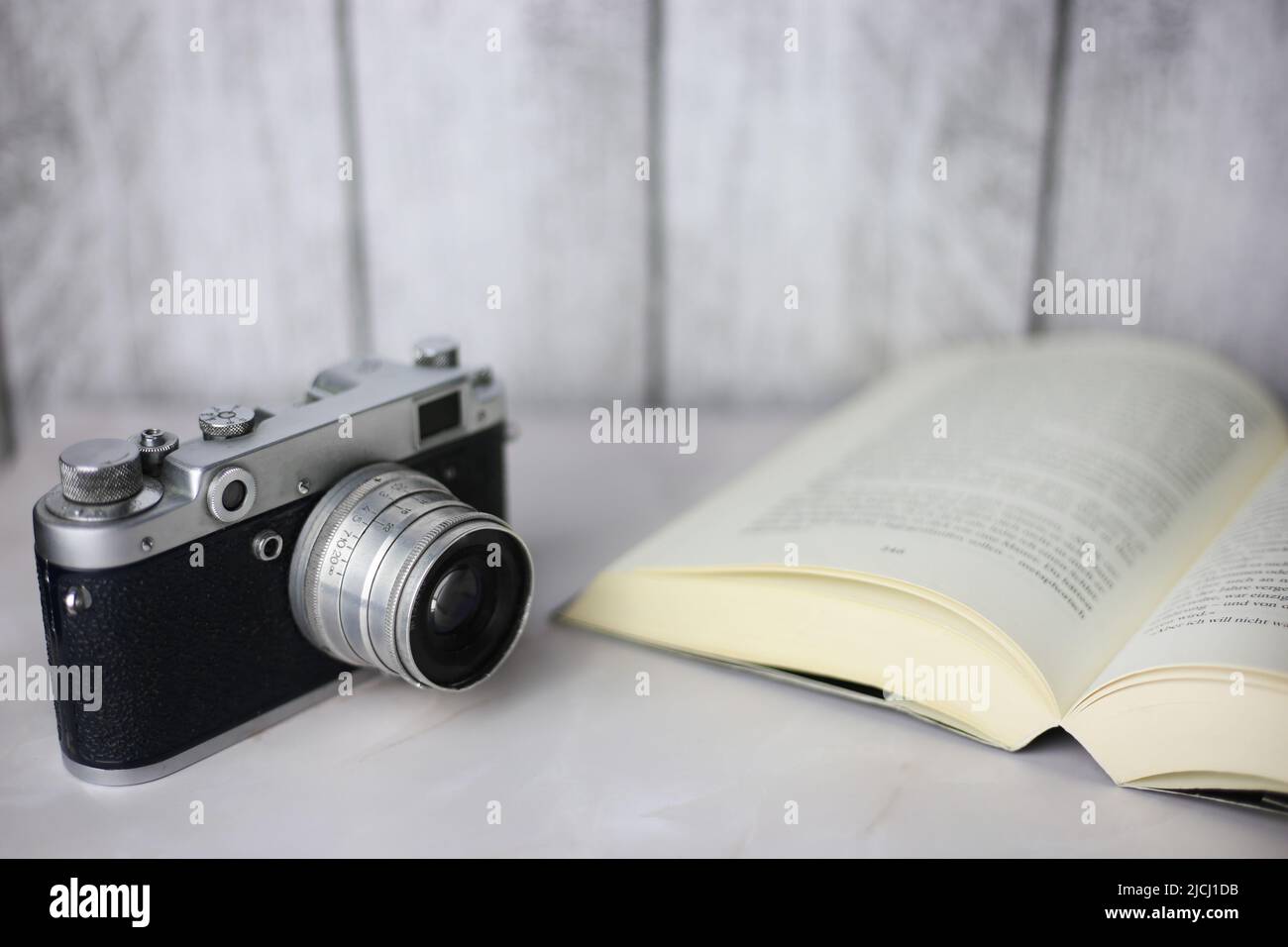 Vintage-Kamera neben einem offenen Buch auf hellem Hintergrund Stockfoto
